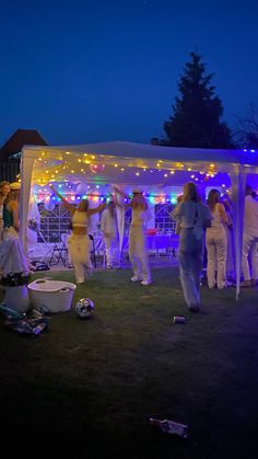 a group of people standing under a tent with lights on it's sides at night