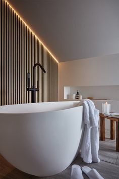 a large white bath tub sitting next to a wooden table with candles and towels on it