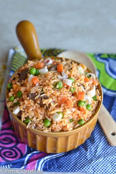 a bowl filled with rice and vegetables next to a wooden spoon on a colorful cloth