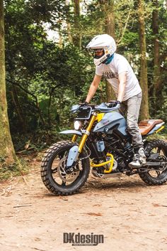 a man riding on the back of a motorcycle down a dirt road in front of trees