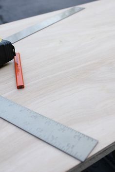 a pair of scissors sitting on top of a piece of wood next to a ruler