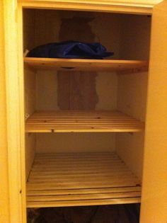 an empty shelf in the corner of a room with clothes on it and a blue bag