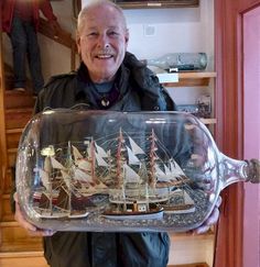 a man holding a glass case with a model ship in it's bottom shelf