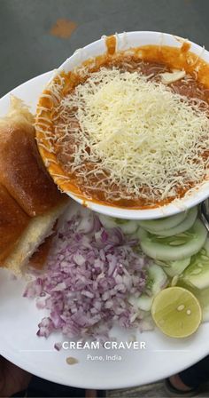 a white plate topped with a bowl of soup next to bread and onion wedges