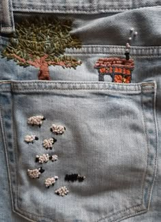 a pair of jeans with sheep in the back pocket and trees embroidered on the side