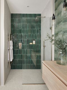 a bathroom with green tiles on the shower wall and wooden countertop, along with a plant in a glass vase