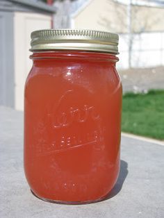 a mason jar filled with liquid sitting on top of a cement surface next to a house