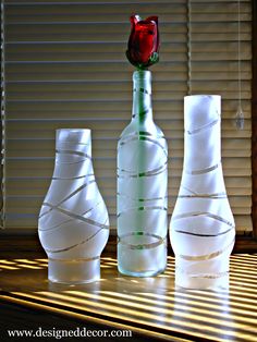 three white vases sitting on top of a wooden table next to a red rose