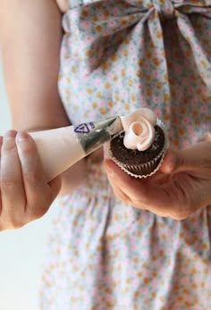 a woman holding a cupcake with icing on it and a pair of scissors in her hand