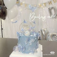 a blue and white birthday cake sitting on top of a table next to foil balloons