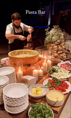 a man standing over a table filled with plates and bowls full of food next to lit candles