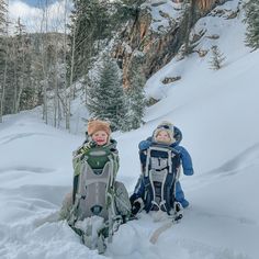 two children sitting in the snow with backpacks