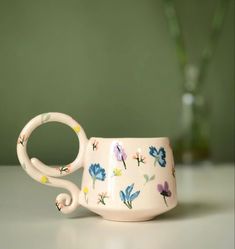 a white cup with flowers painted on the outside and inside, sitting on a table