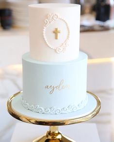 a white and gold wedding cake with a cross on the top is sitting on a stand