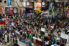 a large group of people standing around in a room with posters on the walls and banners hanging from the ceiling