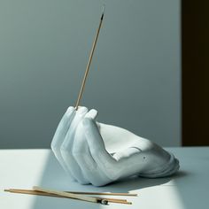 a white sculpture with two hands holding a toothpick and an object next to it