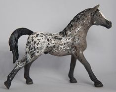 a toy horse is shown on a gray background with white spots and black legs,