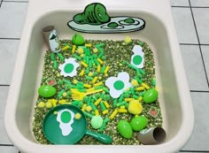 a bathtub filled with lots of green and yellow toys on top of a tiled floor