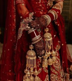 a woman in a red bridal outfit with gold jewelry on her arm and hands