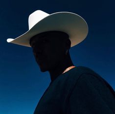 a man wearing a white cowboy hat in front of a blue sky with no clouds