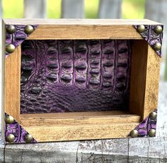 a wooden frame with purple alligator skin and brass studs on the edges is sitting on a piece of wood