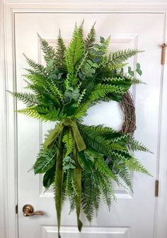 a wreath is hanging on the front door with green leaves and greenery around it