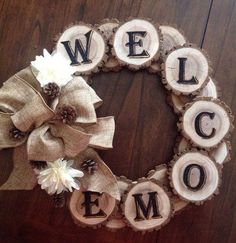 a wreath made out of wood slices with the word welcome on it and white flowers