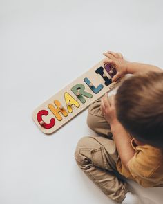 a young child playing with a wooden name puzzle on top of a white floor next to the word charii