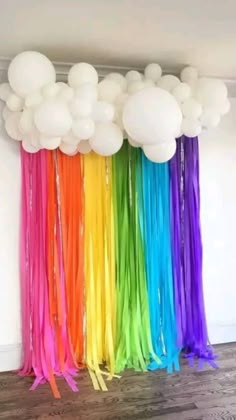 balloons and streamers are hanging from the ceiling in front of a rainbow colored wall