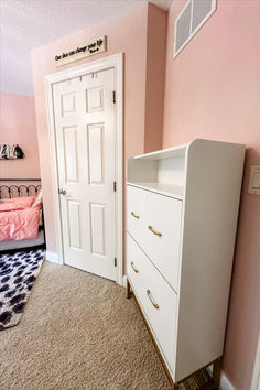 a white dresser sitting next to a bed in a pink room with a black and white rug on the floor