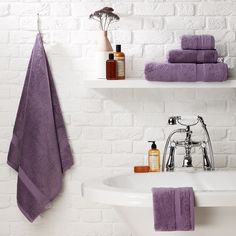 a bathroom with white brick walls and purple towels on the shelf above the bathtub