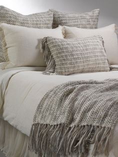 a bed covered in pillows and blankets with fringes on the pillowcase, along with two throw pillows