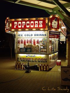 an ice cold drink stand is lit up at night with lights on the roof and signs above it