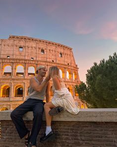 a man and woman are sitting on a wall in front of the colossion