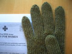 a pair of green knitted gloves sitting on top of a table next to a paper