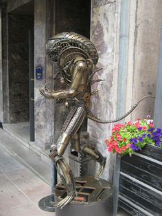 a statue of an alien standing next to a planter with flowers in front of it