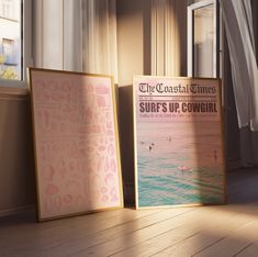 two framed posters sitting on the floor next to each other in front of a window