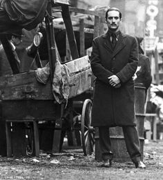 black and white photograph of man standing in front of horse drawn wagon