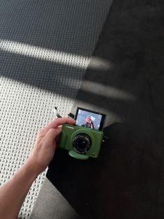 a person holding a green camera on top of a black table next to a white wall