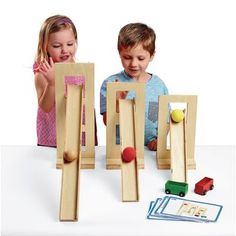 two children playing with wooden toys on a white table and one child is looking at it