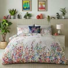 a bed with colorful comforters and pillows in a room filled with potted plants