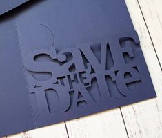 a piece of paper cut into the shape of a save the date sign on a wooden table