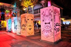 brightly lit booths with faces on them in front of palm trees and buildings at night