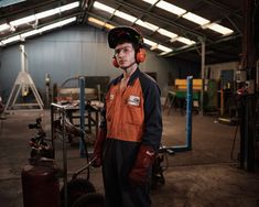 a man in an orange and black work shirt is standing next to a machine with headphones on