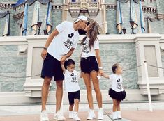 a man and two children standing in front of a castle with mickey mouse shirts on