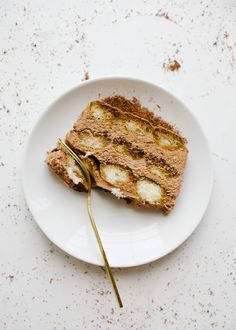 a piece of bread on a white plate with a gold fork next to it,