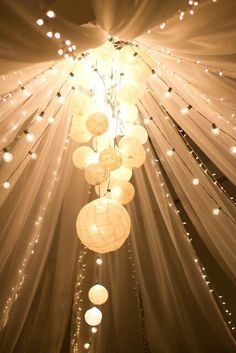 some lights hanging from the ceiling in a room with white drapes and string lights