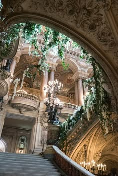 an ornate staircase with chandeliers and greenery on the ceiling in a building