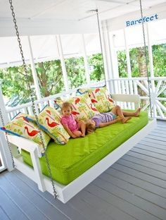 a white porch swing bed with green cushions on the front and back, hanging from a chain