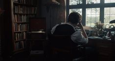 a woman sitting at a desk in front of a bookcase talking on the phone